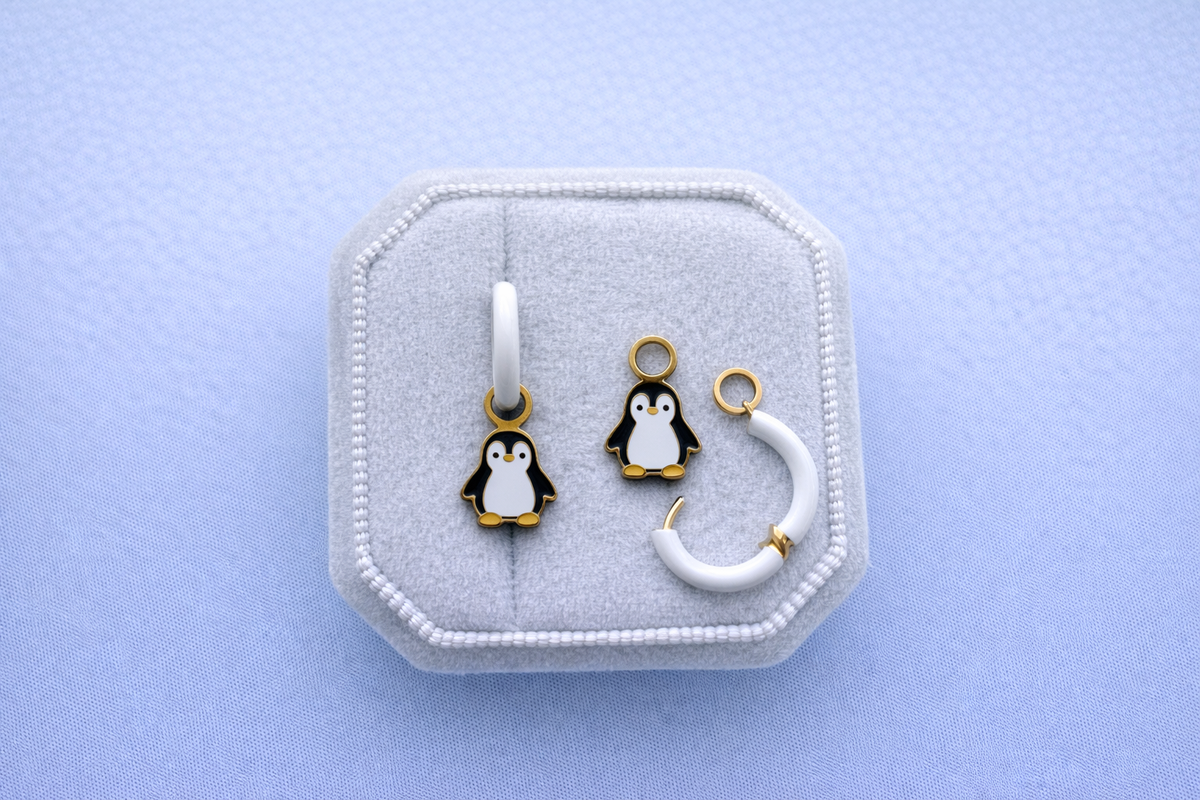 Jewelry set with penguin charms on white huggie hoops on a white jewelry box on a light blue background