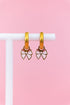 Set of light pink bow charms on gold huggie charms hanging on a white jewelry stand against a light pink background