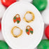 Plaid bow huggie charms and 8mm gold huggie hoops laying on a white jewelry cushion on a red, green, and white background