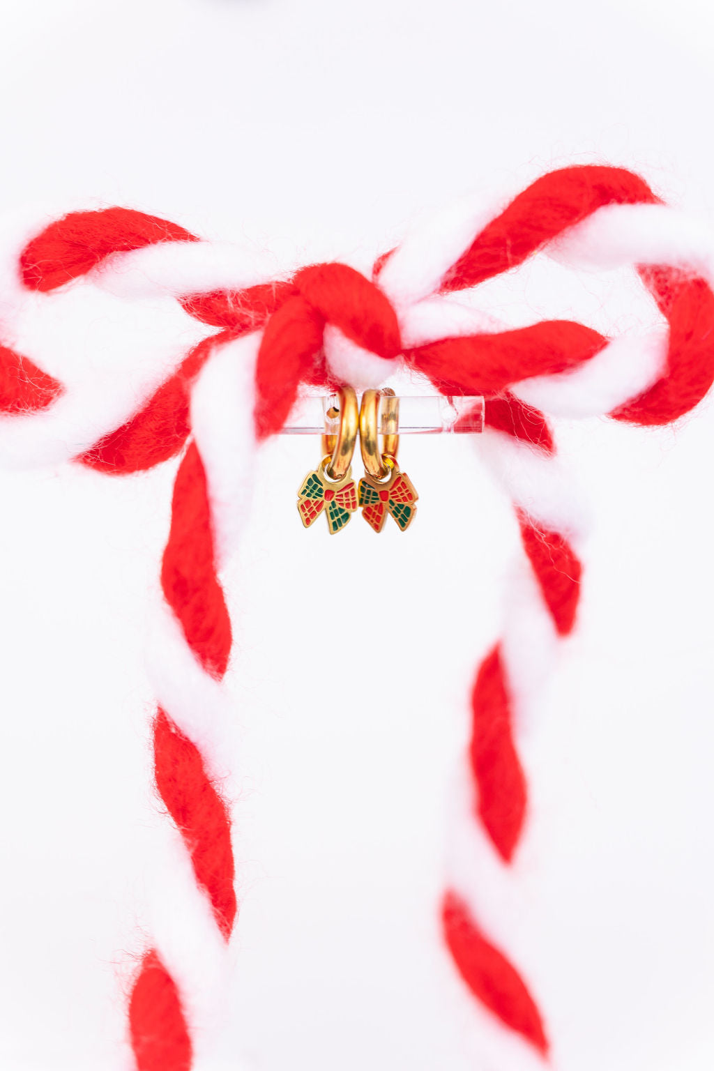 Plaid bow huggie charms on 8mm gold huggie hoops hanging on a clear jewelry stand with a candy cane colored bow against a white background