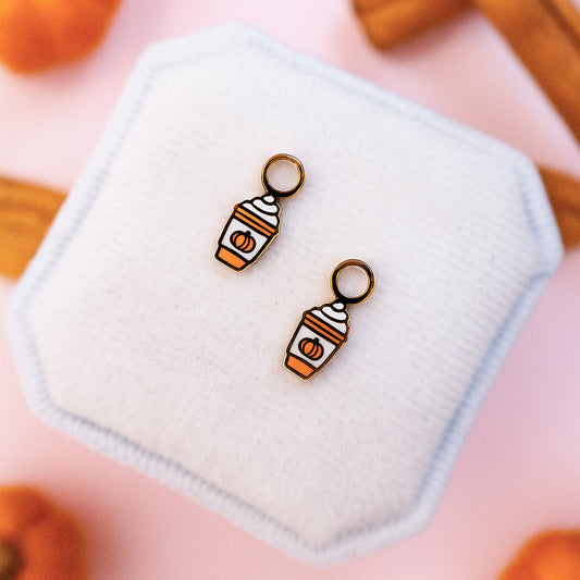 Pair of earrings on a hexagonal white stand with pumpkins and cinnamon sticks in the background.