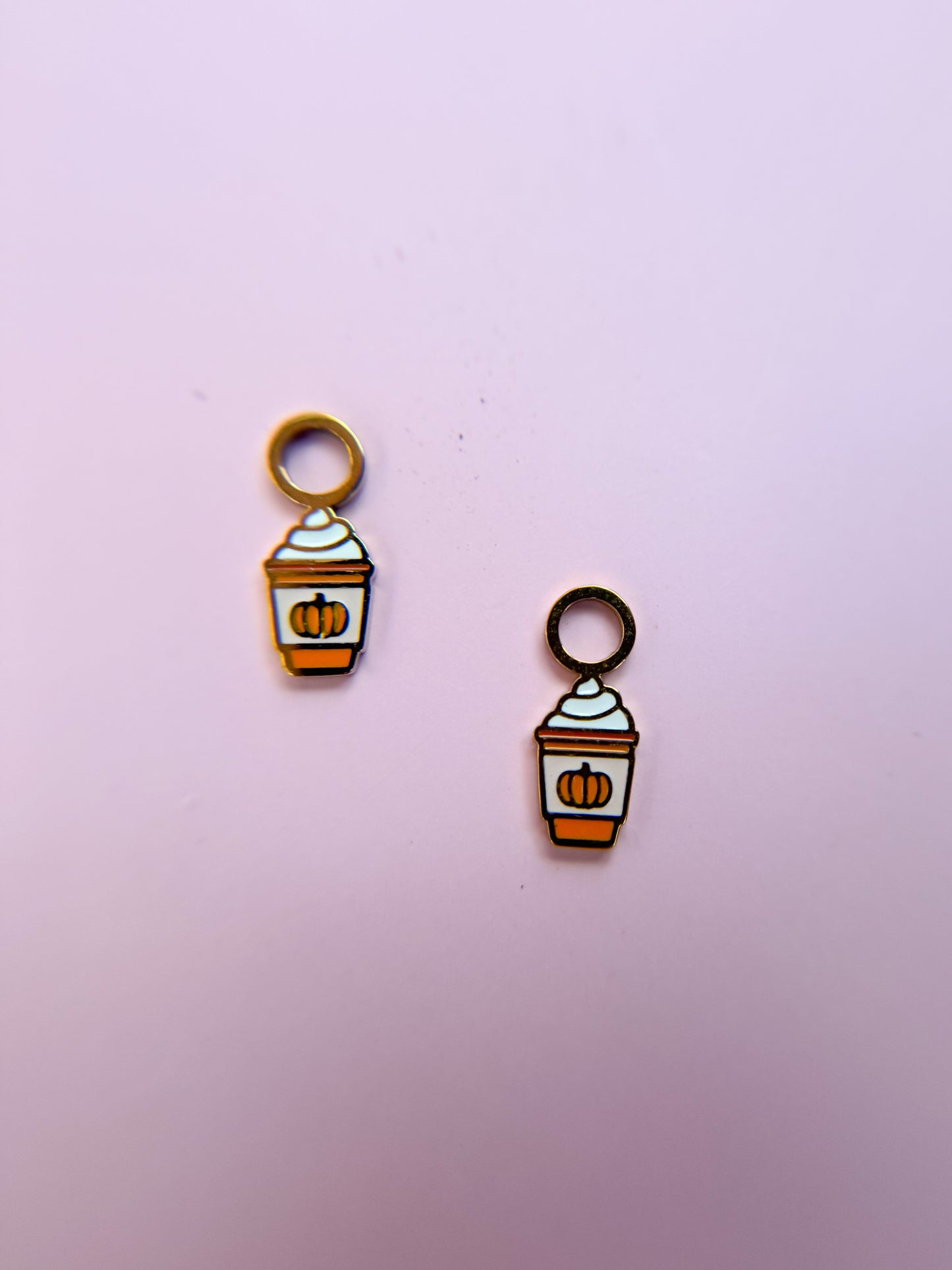 Two pumpkin spice latte-themed charms on a pink background