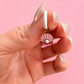 Hand holding a seashell-shaped earring with a pearl on a pink background