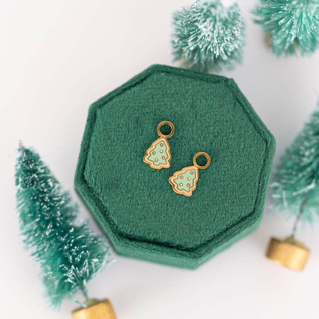 Christmas tree sugar cookie Huggie Charms on a green jewelry box against a white background with mini scrub brush Christmas trees in the background 