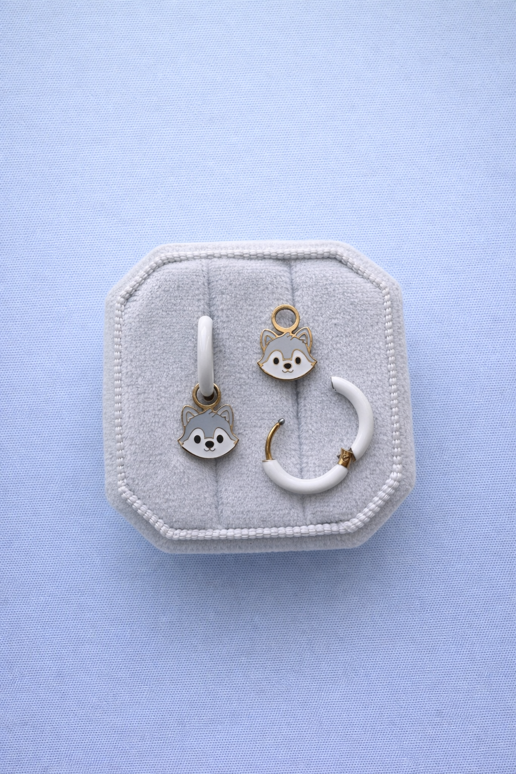 Wolf shaped charms on white huggie hoops on a white jewelry box against a light blue background