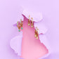 Gold hoop earrings with gemstones on a pink and purple background