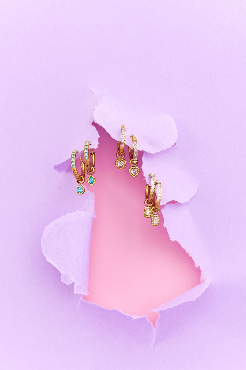 Gold hoop earrings with gemstones on a pink and purple background