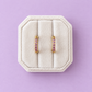 Lavender cz huggie hoops on a white jewelry box on a lavender background