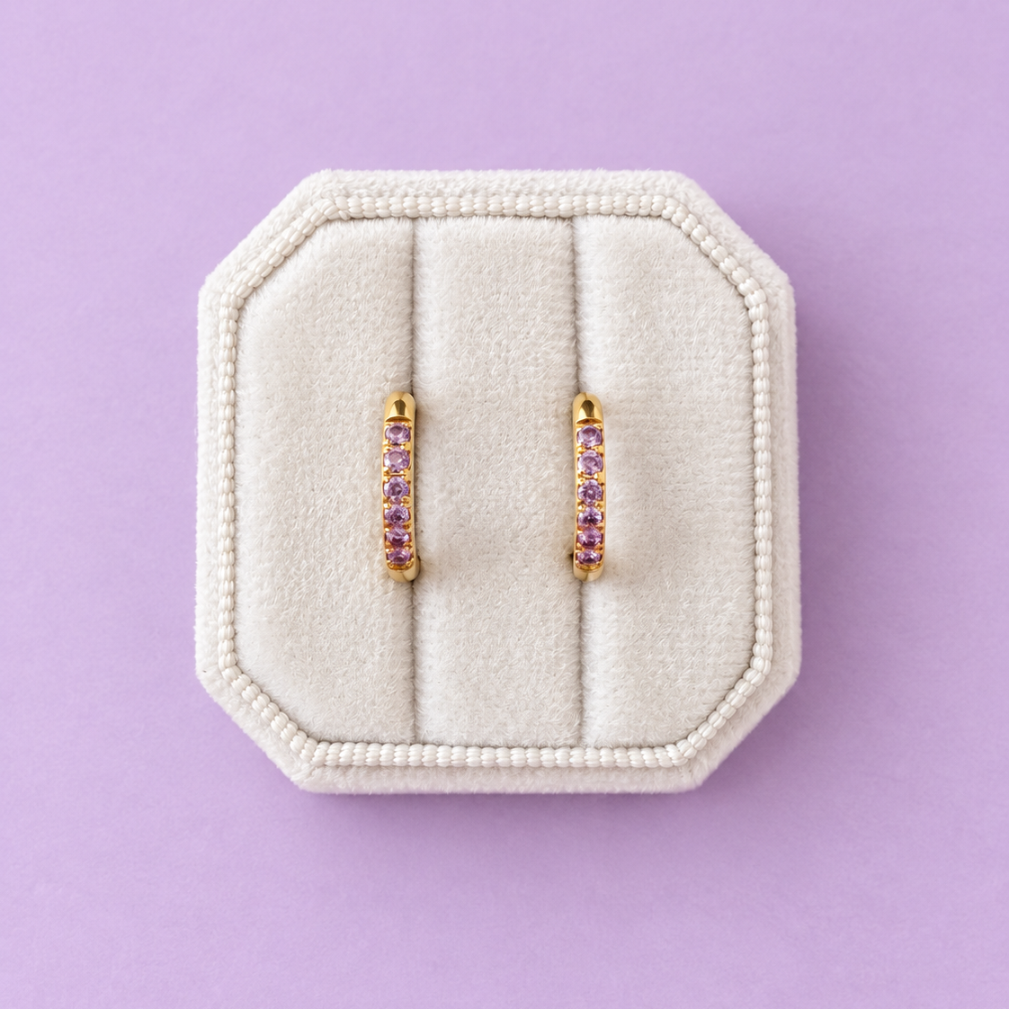 Lavender cz huggie hoops on a white jewelry box on a lavender background