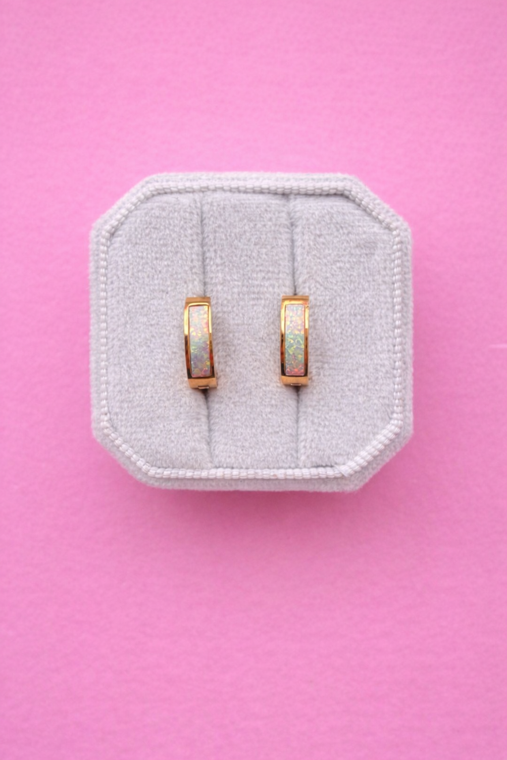 Chunky gold hoops with Opal accents on a white jewelry box against a light pink background