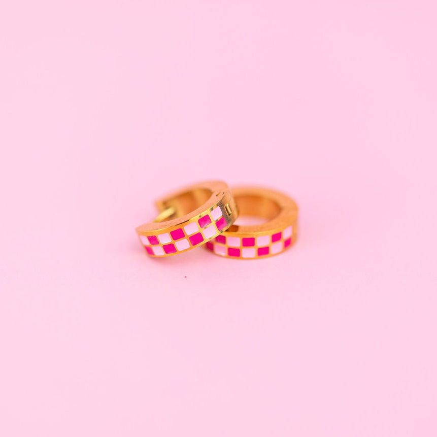 Two pink checkered chunky huggie hoops on a light pink background