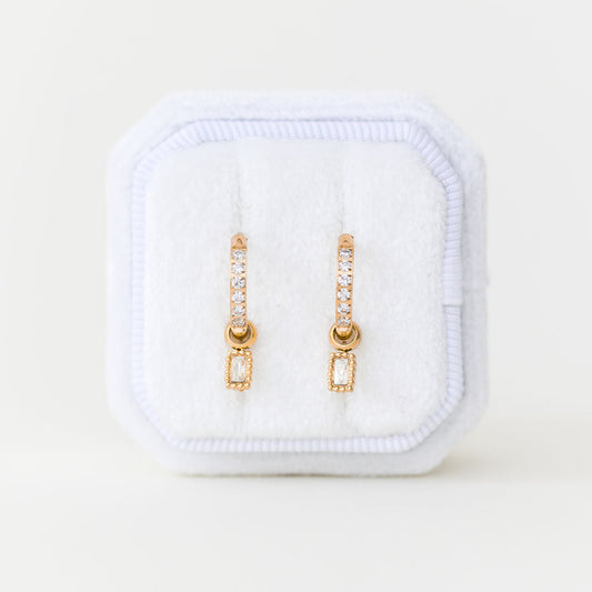 Gold earrings in a white jewelry case on a light beige background