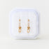Gold cz stone huggie hoops with an emerald shape cz charm in a white jewelry box on a light beige background