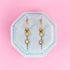 CZ Huggie hoops with emerald shaped charms and emerald shaped studs on a teal jewelry box on a light pink background