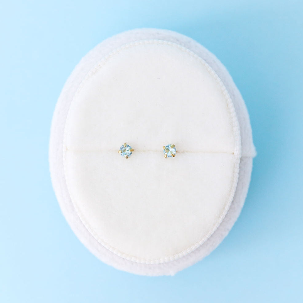Pair of stud earrings on a white cushion against a light blue background