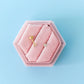 Pink hexagonal jewelry box with gold earrings on a light blue background