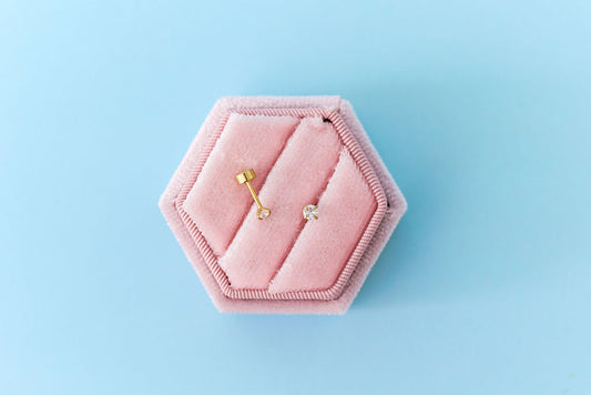Pink hexagonal jewelry box with gold earrings on a light blue background