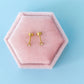 Gold earrings on a pink hexagonal jewelry box against a light blue background