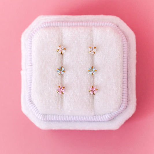 Set of earrings on a white jewelry display with a pink background