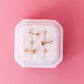 Set of gold earrings on a white cushion with a pink background