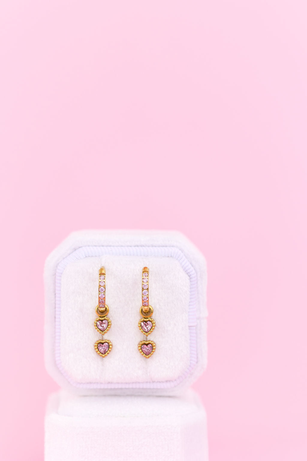 Heart-shaped earrings in a white box on a pink background