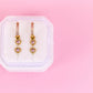 Pair of heart-shaped earrings on a white jewelry pouch against a pink background