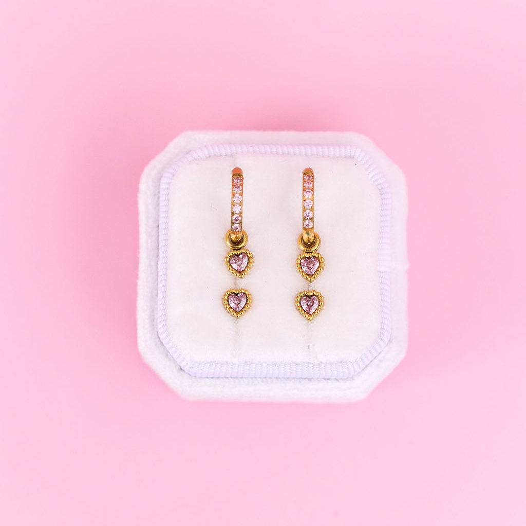 Heart-shaped earrings in a white box on a pink background