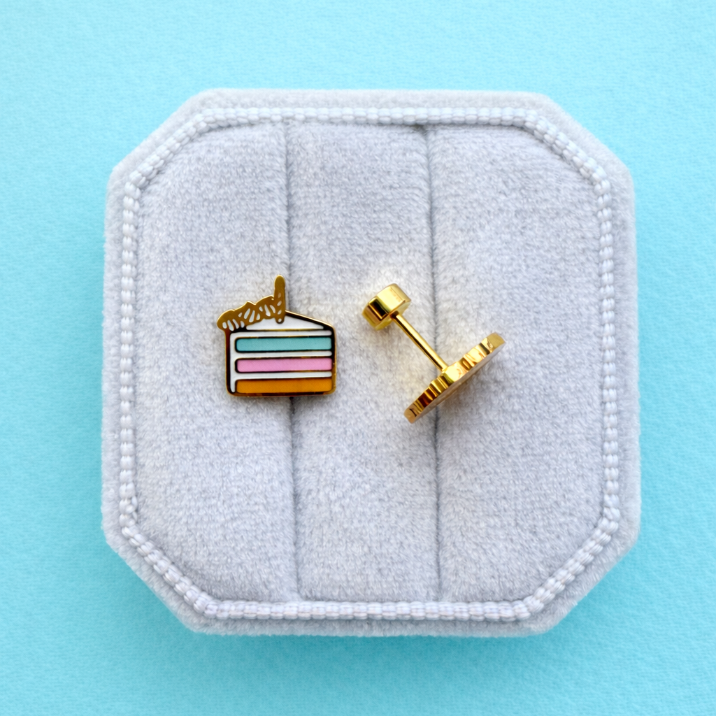 Birthday cake slice stud earrings on a white jewelry box on a light blue background