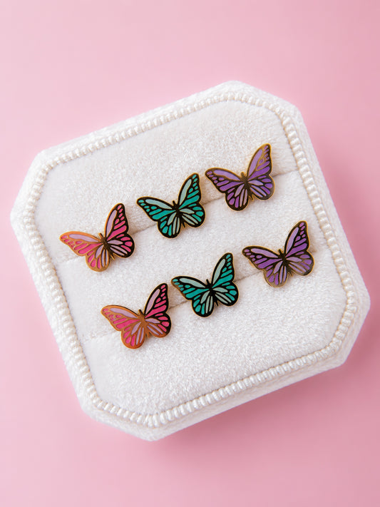 Set of three butterfly enamel studs in pink, purple and teal in a white jewelry box on a light pink background