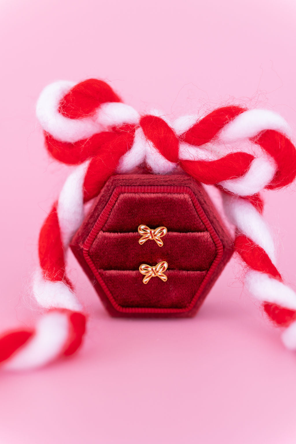 Candy cane bow studs in a red jewelry box against a light pink background with a candy cane colored bow