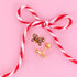 Candy cane bow flat back studs against a light pink background with a candy cane colored string in the shape of a bow