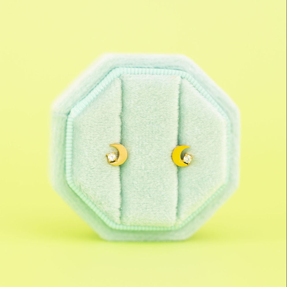 Gold crescent moon cz studs on a teal jewelry box against a light neon green background