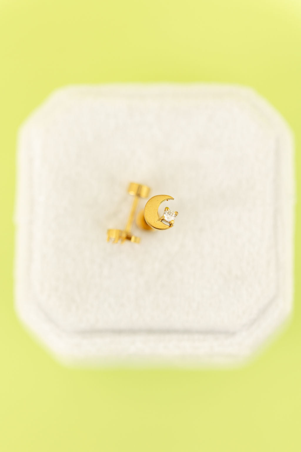 Gold crescent moon cz studs with flat backs on a white jewelry box against a light neon green background