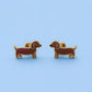 A pair of dachshund-shaped stud earrings in brown enamel with gold-tone metal outlines, displayed on a light blue background.