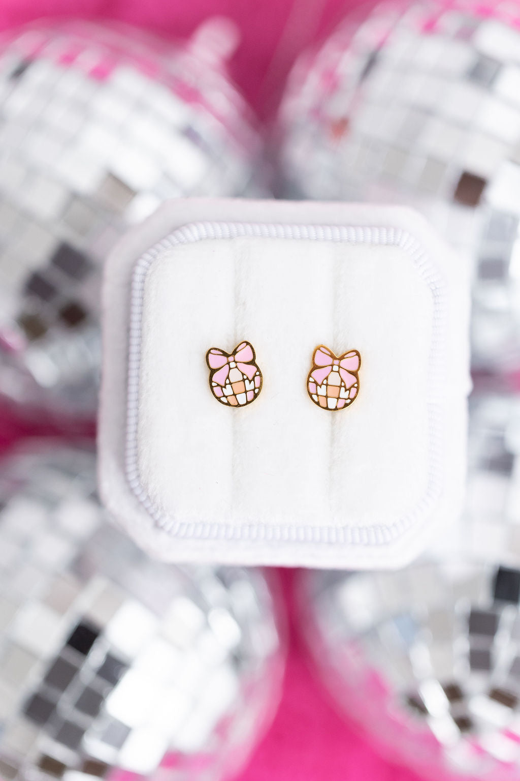 Disco balls with pink bows studs on a white jewelry box laying on disco balls on a hot pink background
