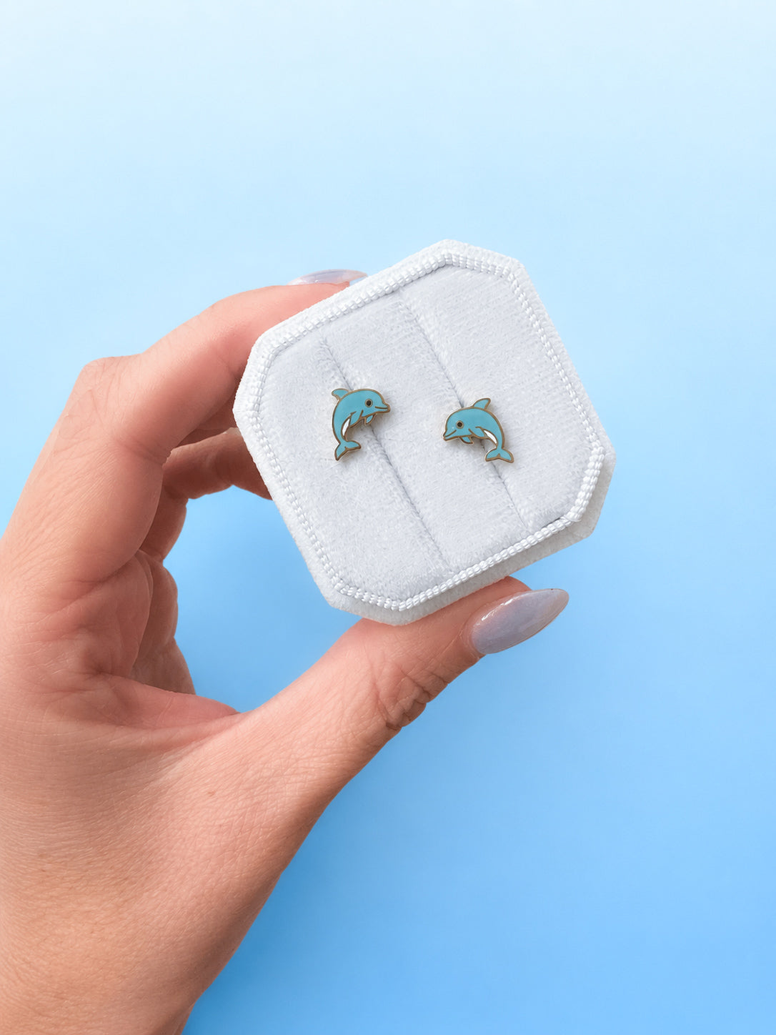 Hand holding a white jewelry box with blue dolphin designs against a light blue background