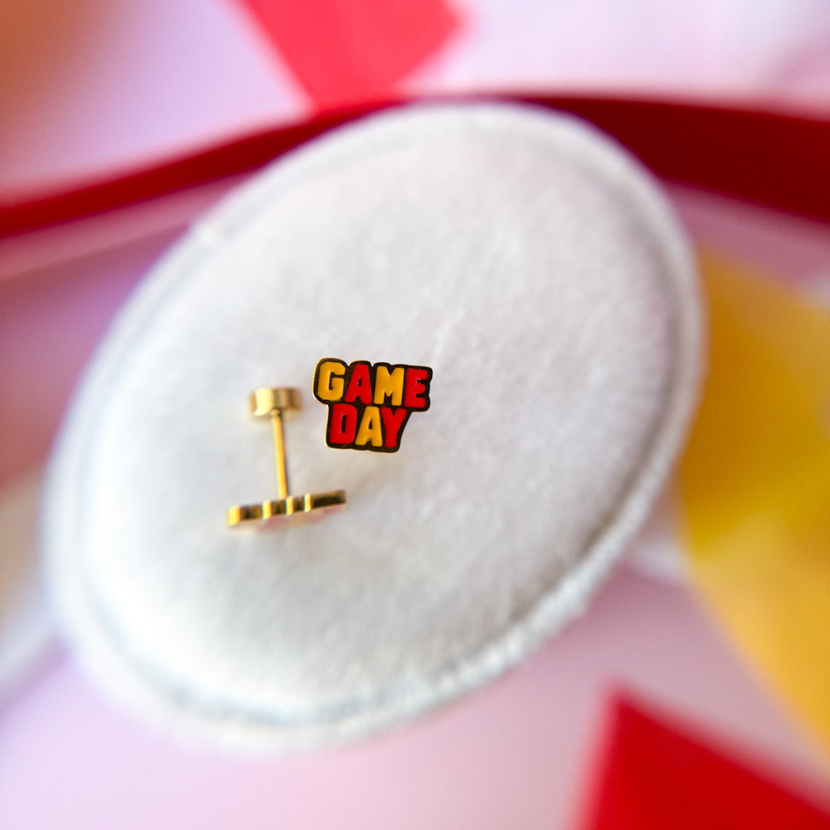 Round white jewelry box with 'GAME DAY' gold earrings on a colorful background