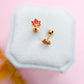 Two gold and pink maple leaf earrings on a hexagonal white stand against a pink background.
