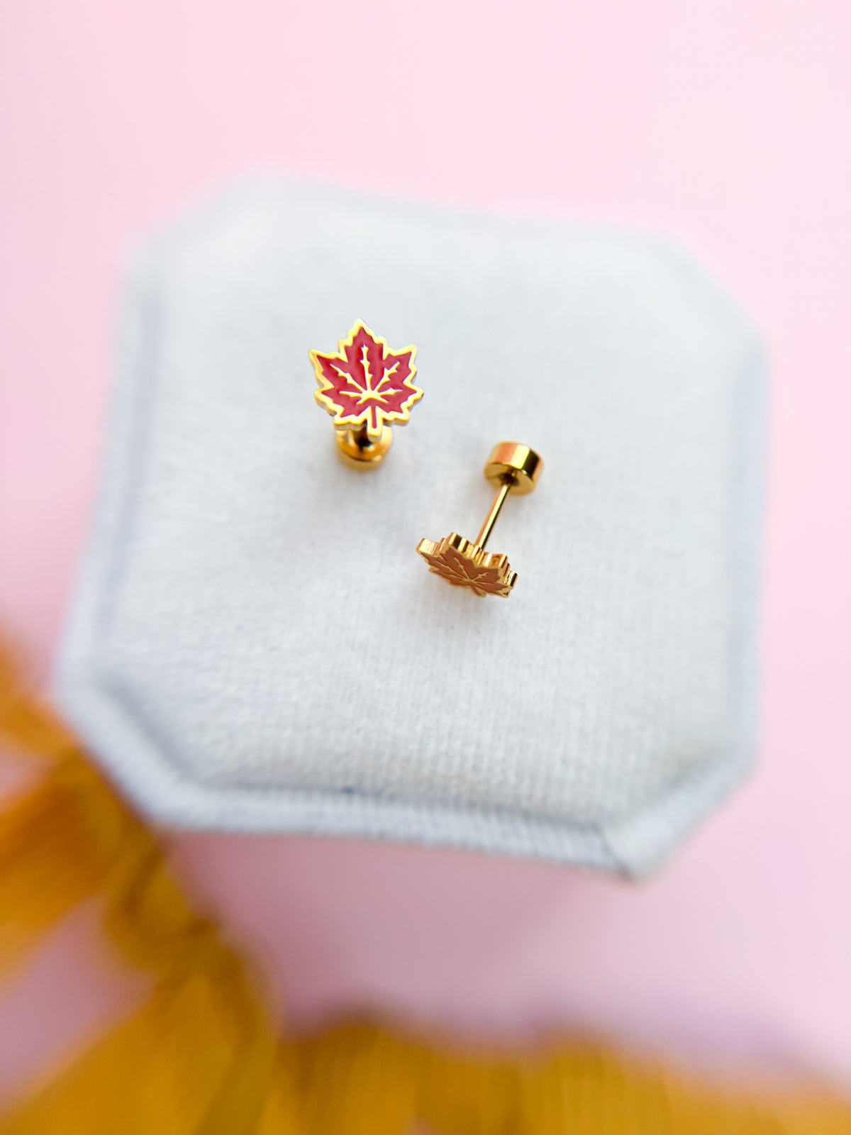 Red and orange maple leaf earrings with flat backs on a white jewelry box against a pink background