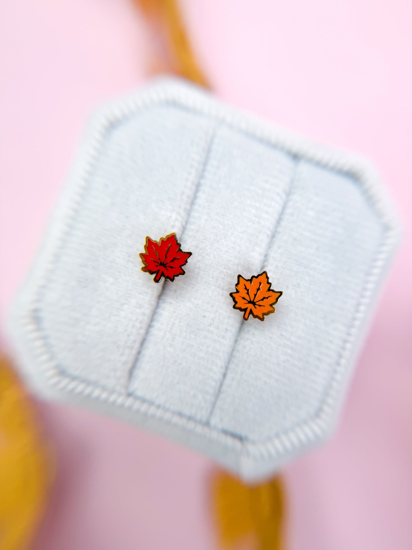 Two maple leaf earrings on a white card with a pink background