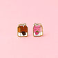 Two milk carton shaped stud earrings. One chocolate, one strawberry on a light pink background