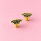 A pair of gold butterfly-shaped stud earrings with black enamel detailing, displayed on a solid pink background.