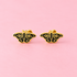 A pair of gold butterfly stud earrings with black enamel detailing, displayed on a solid pink background.