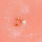 Two small gold mushroom earrings on a pink textured background