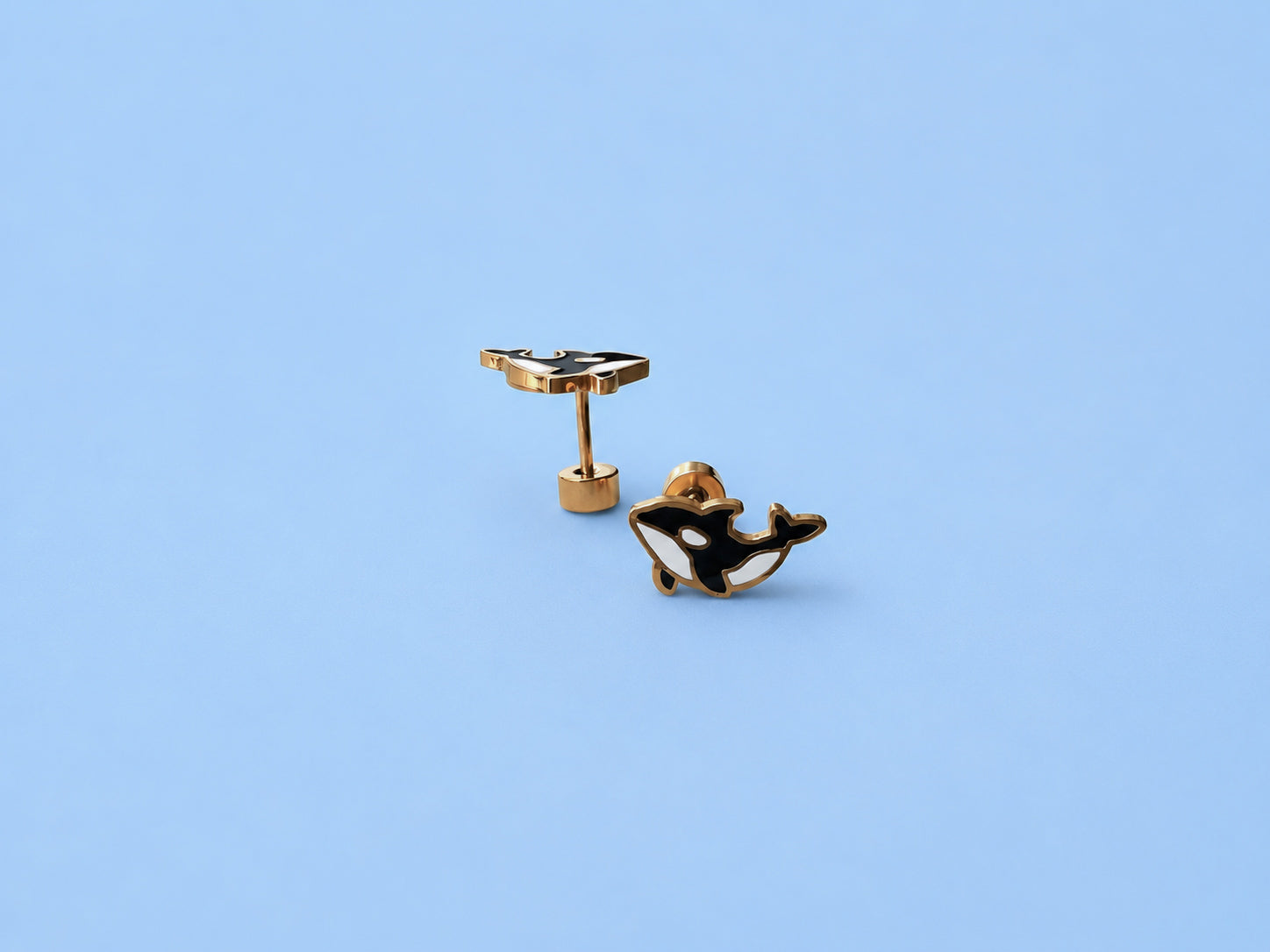 Black and gold whale-shaped earrings on a light blue background