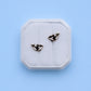 Pair of whale-shaped earrings on a white hexagonal stand against a light blue background