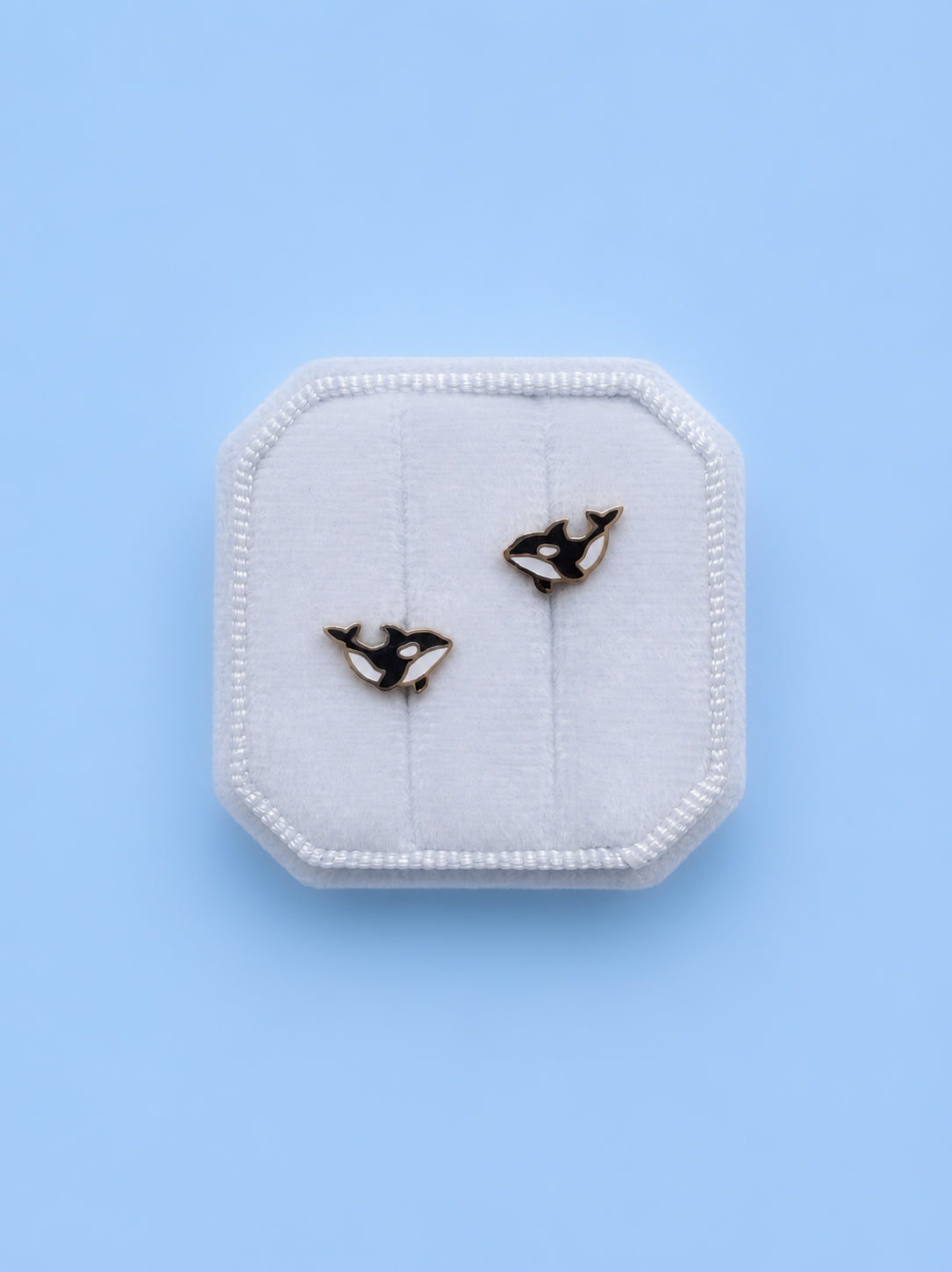 Pair of whale-shaped earrings on a white hexagonal stand against a light blue background