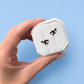 Hand holding a white hexagonal jewelry box with whale earrings on a light blue background