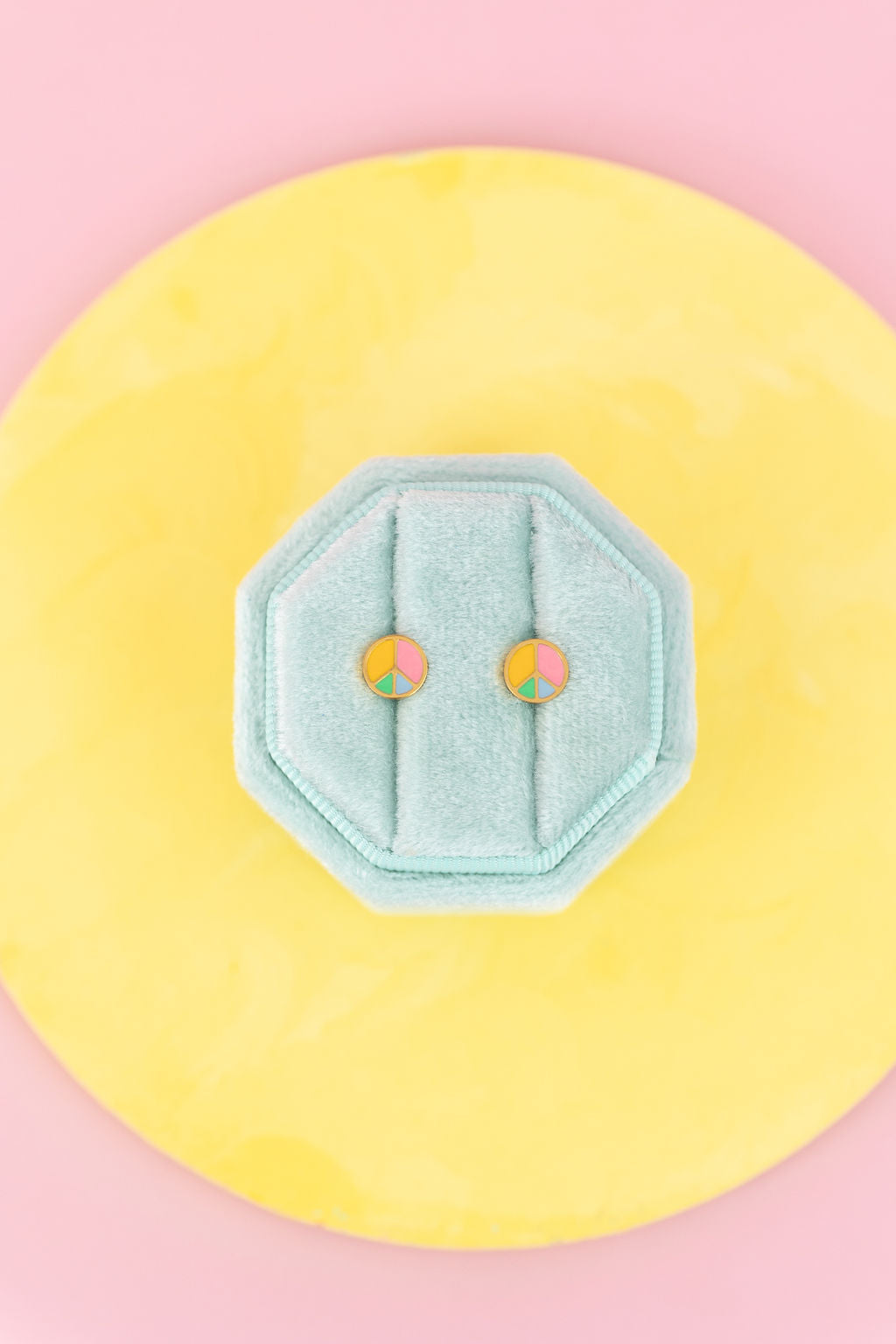 Peace Sign Stud Earrings on a teal jewelry box on a light yellow and light pink background