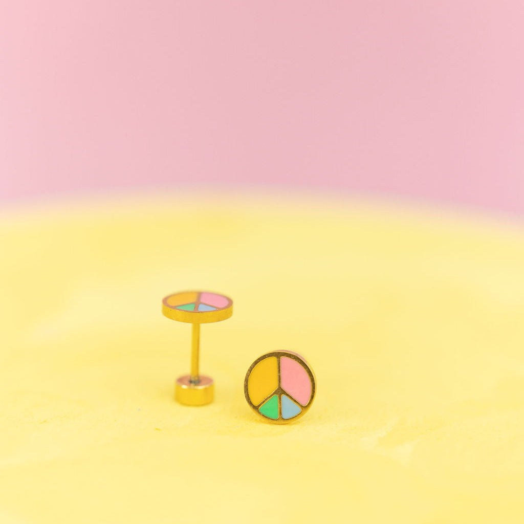 Peace Sign Stud Earrings against a light yellow and light pink background